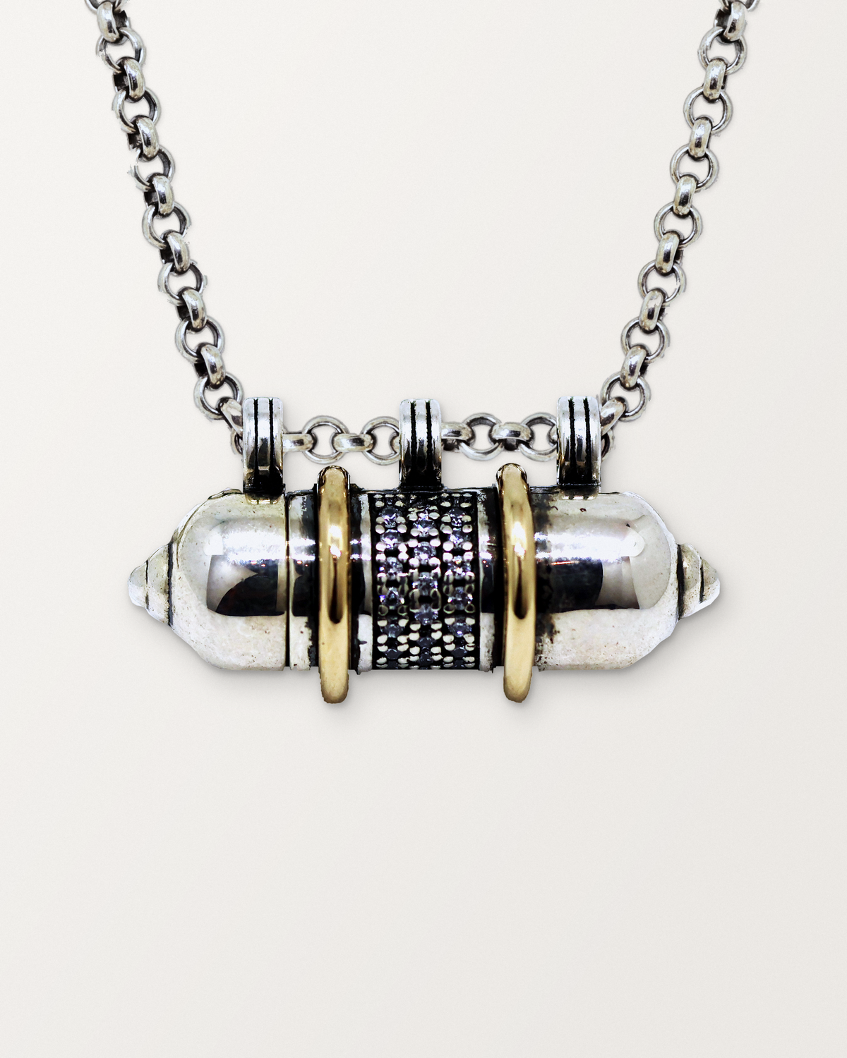 Close-up of the closed sterling silver Vidya amulet necklace with 14K yellow gold bands, front, on a warm bone-white background.