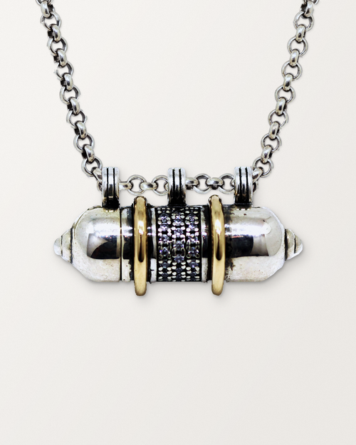 Close-up of the closed sterling silver Vidya amulet necklace with gold bands, front, on a warm bone-white background.