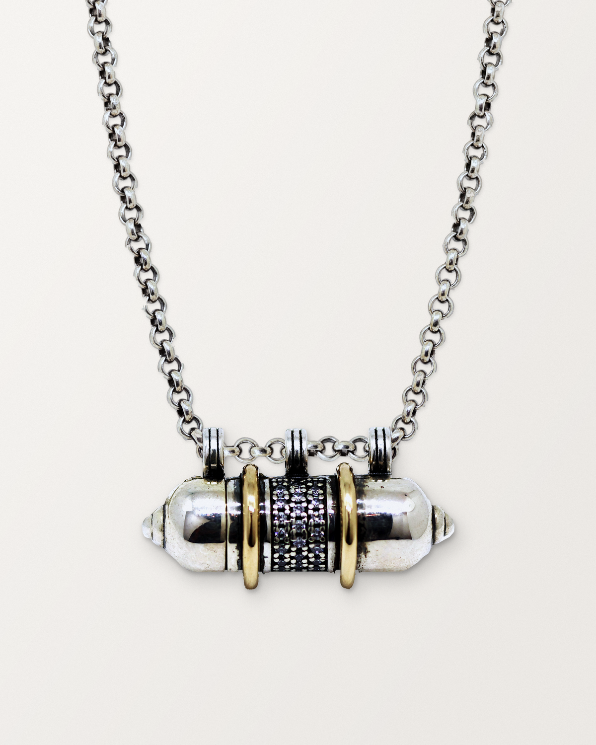 Sterling silver Vidya amulet necklace with gold bands, closed, hanging on its chain against a warm bone-white background.