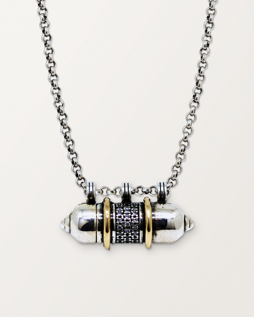 Sterling silver Vidya amulet necklace with gold bands, closed, hanging on its chain against a warm bone-white background.