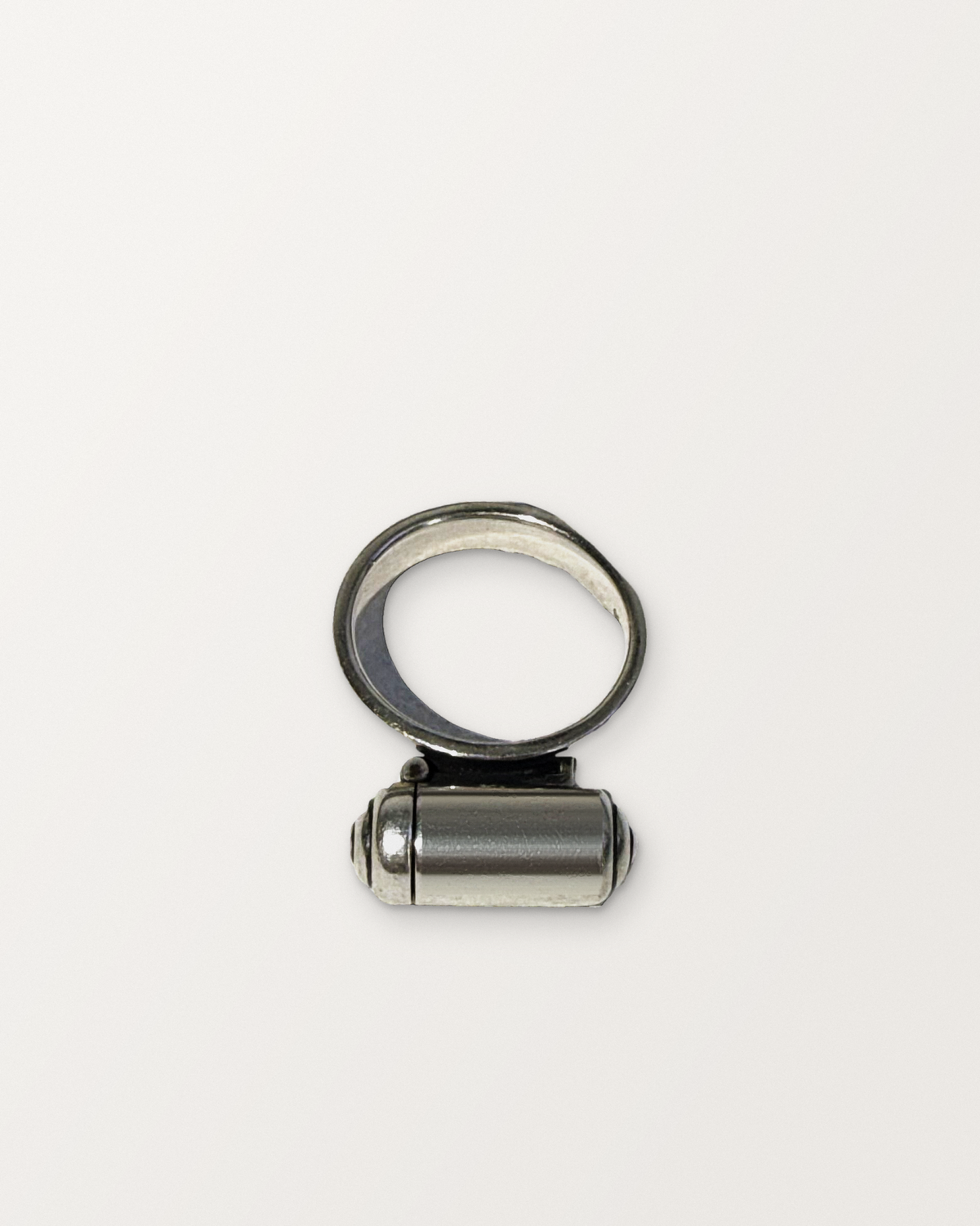 Sterling silver VRAT ring amulet, closed, on a warm bone-white background.