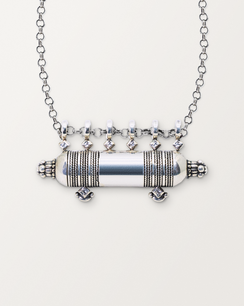 Close-up of the closed sterling silver Yemen Wedding amulet necklace, front, on a warm bone-white background.