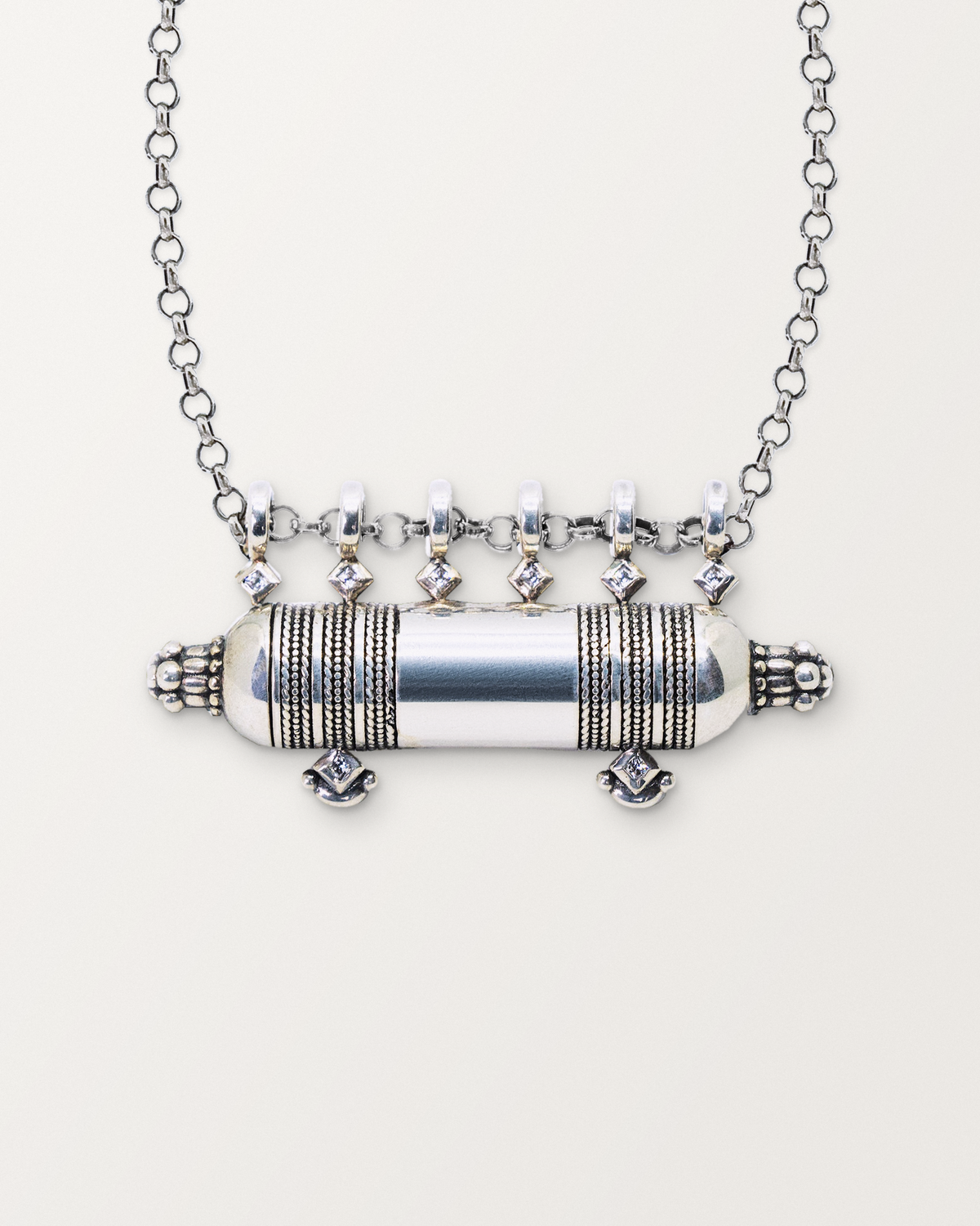 Close-up of the closed sterling silver Yemen Wedding amulet necklace, front, on a warm bone-white background.