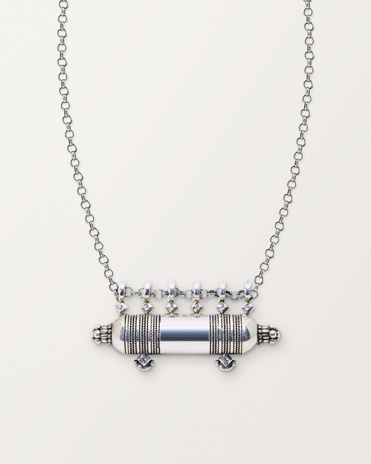 Sterling silver Yemen Wedding amulet necklace, closed, on a warm bone-white background, chain exiting the top of frame.